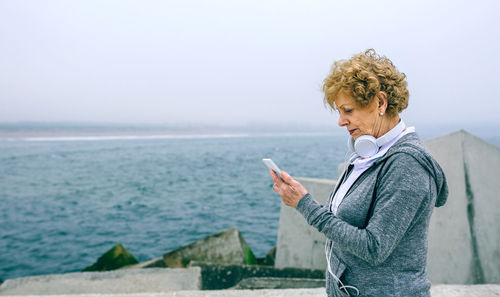 Side view of young woman using smart phone against sea