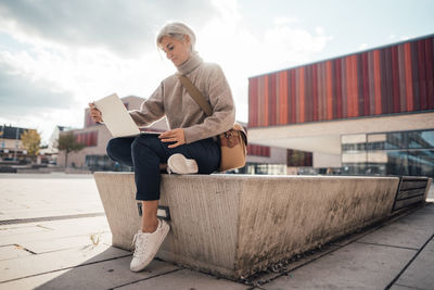 Businesswoman using laptop sitting at seat on footpath