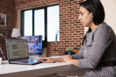 Side view of young woman using laptop while sitting at office