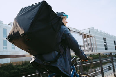 Female delivery person carrying backpack and cycling on street in city