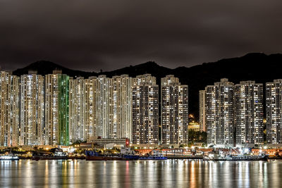 Illuminated city by sea against sky at night