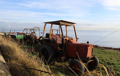 Abandoned car on field by sea against sky