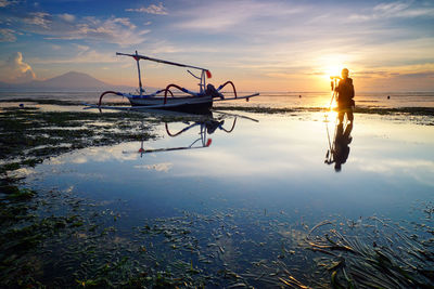 People fishing on beach against sky during sunset