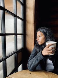Young woman looking away while sitting on window