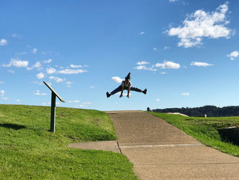 Full length of woman jumping over footpath against sky