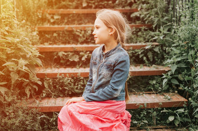 Happy smiling candid eight year old kid girl sits on staircase in nature. prepubertal children