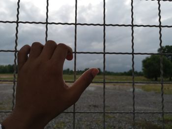 Close-up of hand on metal fence against sky