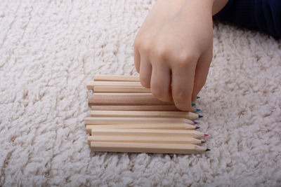 Cropped hands of boy holding colored pencil over carpet