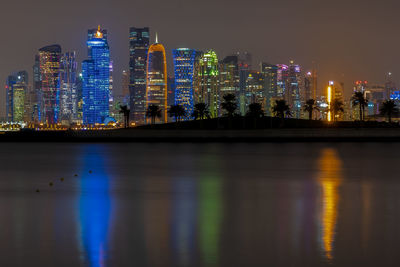 Illuminated buildings by river against sky at night