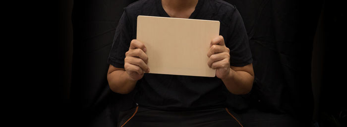 Midsection of man holding blank placard against black background