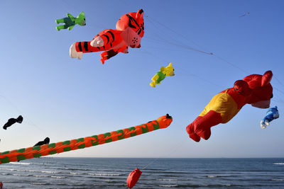 Low angle view of kites flying over sea against clear sky