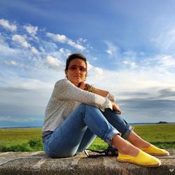 Portrait of woman sitting on retaining wall against sky