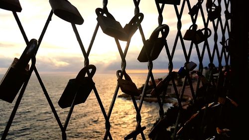 Close-up of silhouette chain hanging on rope against sky during sunset