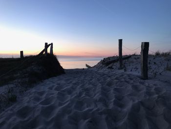 Wooden posts at beach against sky during sunset