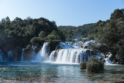 Scenic view of waterfall in forest against clear sky