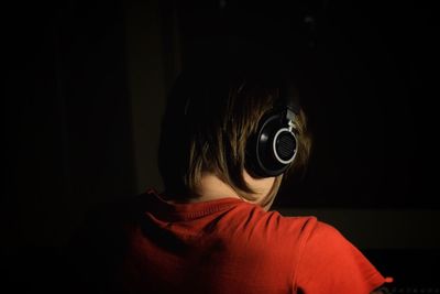 Rear view of teenage boy listening to music against black background