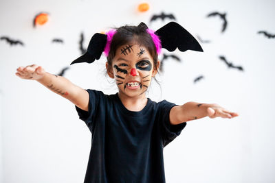 Portrait of cute girl wearing witch costume against wall