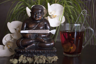 Close-up of buddha statue by drink on table