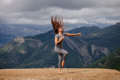 Full length of woman exercising on cliff against sky