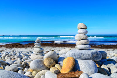 Stack of pebbles on beach against clear blue sky