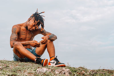 Full length of young man sitting on land against sky