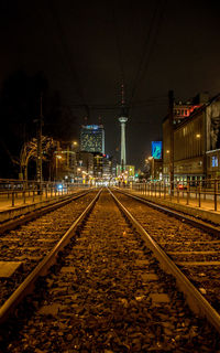 Railroad tracks leading towards illuminated fernsehturm in city at night