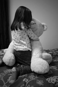 Rear view of girl playing with teddy bear on bed at home