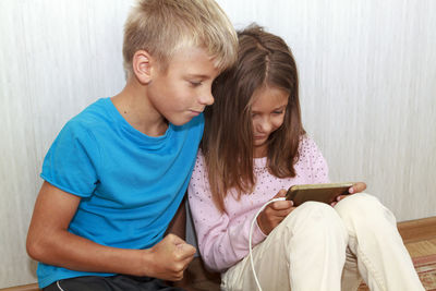 Cute boy and girl using smart phone sitting at home