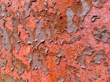 Rusty orange red paint peeling and flaking creating texture and abstract pattern