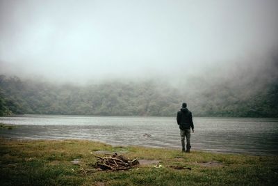 Rear view of man on lake against sky during foggy weather