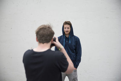 Man photographing model standing against white wall