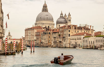 Rear view of man sitting in motorboat in canal against building