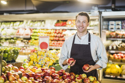 Portrait of smiling mature owner standing at apple stall in grocery store