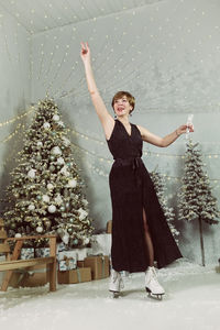 Woman drinks champagne at a skating rink on new year's eve while skating next to a christmas tree