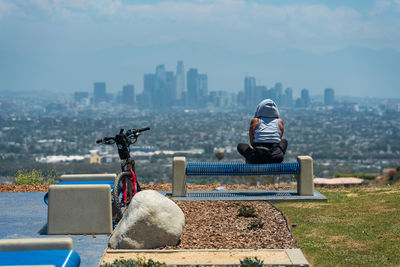 Woman sits on bench and looks at la city scape after a long bike ride