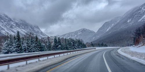 Road by snowcapped mountains against sky during winter