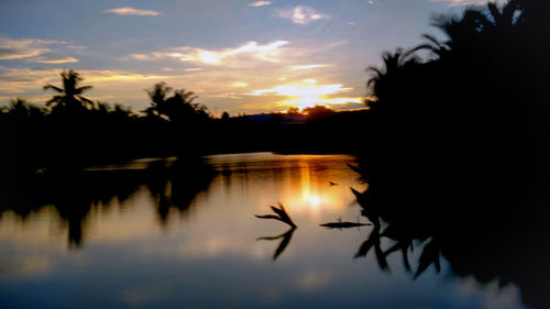 Silhouette trees by lake against sky during sunset