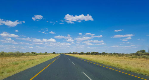 Empty road amidst field against sky