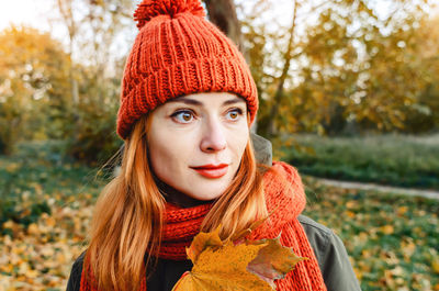 Portrait of mysterious woman with autumn yellow leaf in hand in orange knitted hat and scarf. autumn