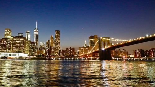 Illuminated bridge over river by buildings against sky at night