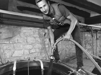 Portrait of worker holding hose while pouring liquid in container at factory