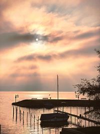 Silhouette sailboats on pier by sea against sky during sunset