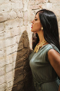 Young woman looking away while standing against wall