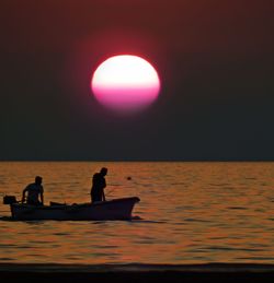 Silhouette people standing on sea against sky during sunset