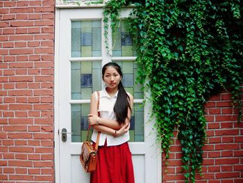 Portrait of young woman standing against closed house door