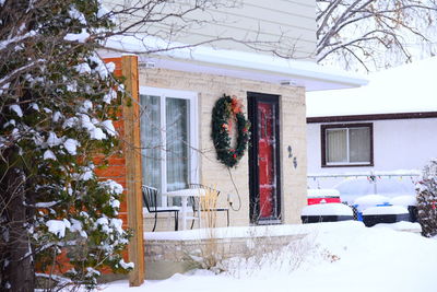 Snow covered house by bare tree against building