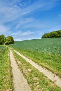 Road passing through field against cloudy sky