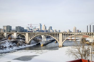 Bridge over river by buildings against sky in city during winter