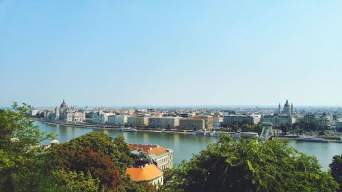 Bridge over river by buildings against clear sky