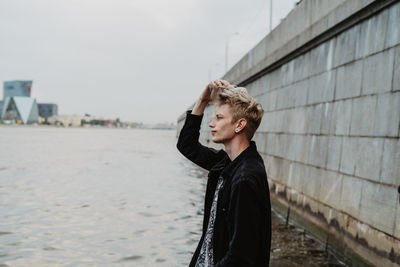 Side view of young woman looking away while standing by sea against sky